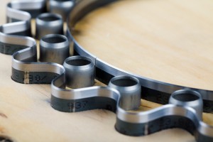 Custom steel rule die with sharp wavy blades and circular punches mounted in a wooden base for precision cutting.