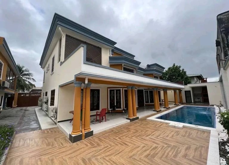 Modern two-story villa with a luxury outdoor swimming pool and wood-tiled patio under a cloudy sky.