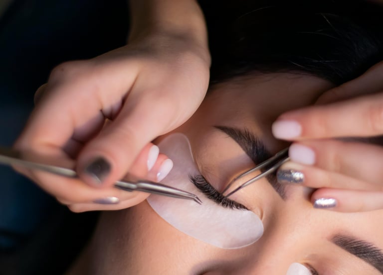 Lashista aplicando extensiones de pestañas a una modelo con parche en cara