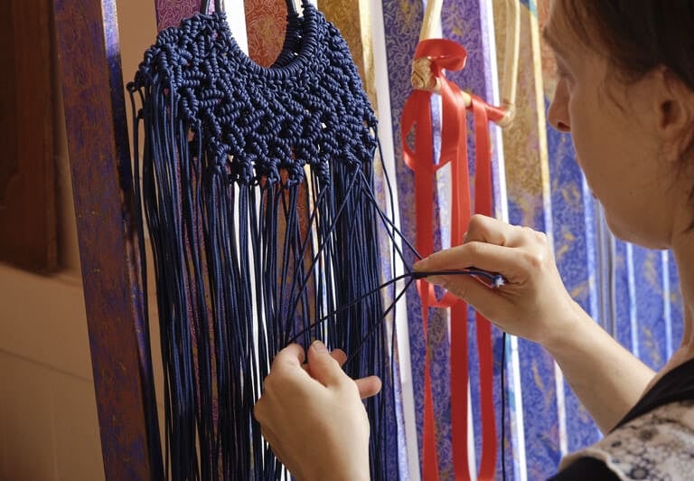 Una artesana tejiendo a mano una bolsa de macramé azul marino