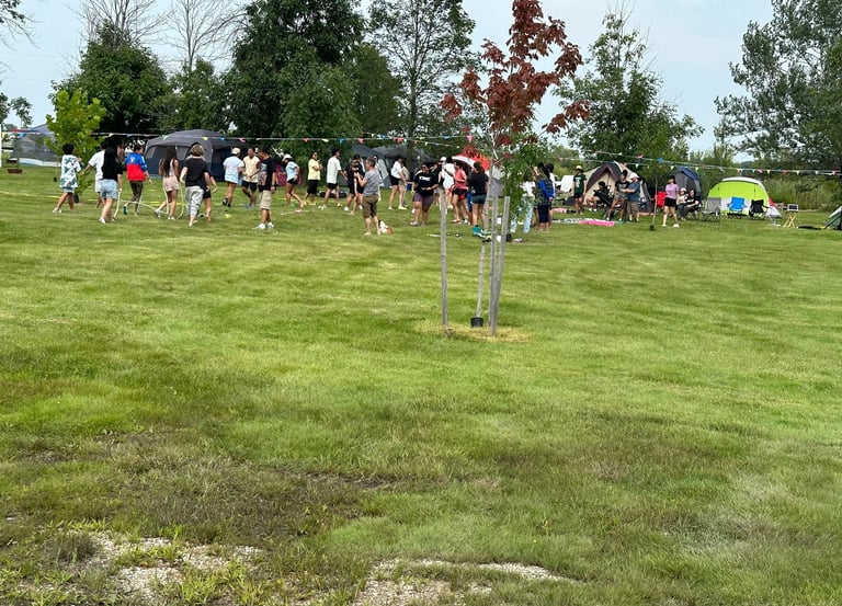 A large group of people participating in outdoor activities at a grassy summer camping retreat.