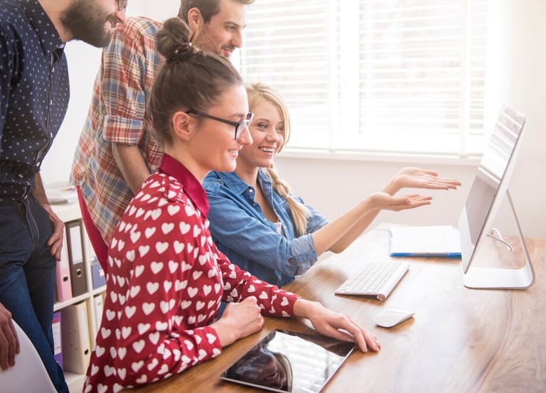 Groupe de personnes souriantes travaillant ensemble sur un ordinateur.