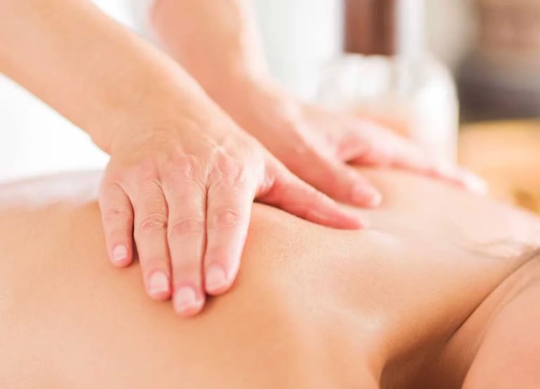 Massage therapist applying pressure to patient's upper back during therapeutic massage.