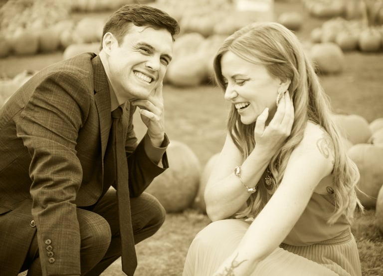 a man and woman in a field of pumpkins smiling in sepia style