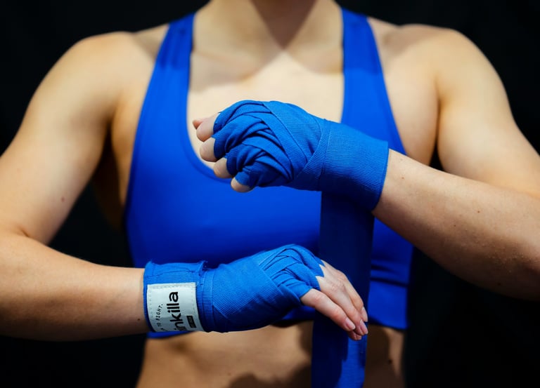 Frau in blauem Sporttop beim Umwickeln ihrer Hände mit Boxbandagen – Symbol für mentales Boxen und Selbstbehauptung