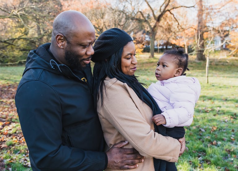 a man and woman holding a baby in a park in Bexley smiling towards the baby