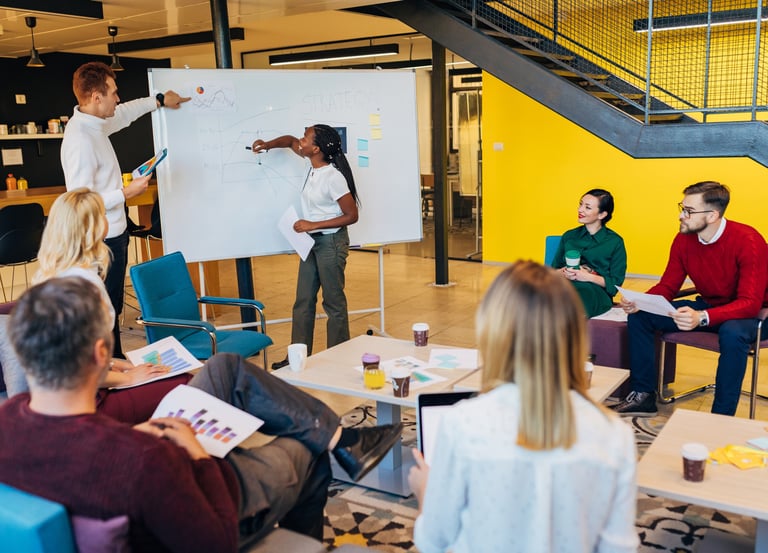 Female business coach giving presentation on whiteboard at team business training