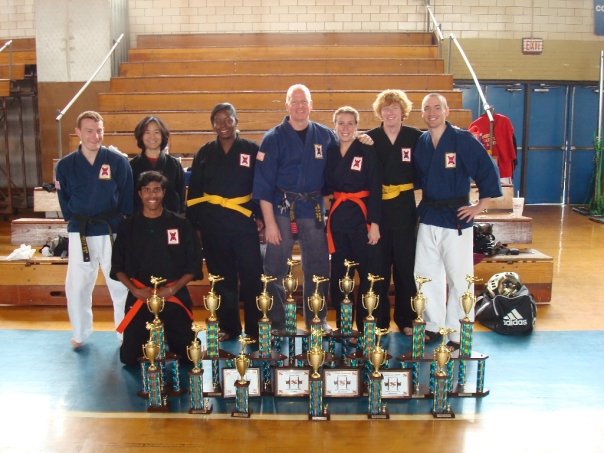 Martial arts team in traditional uniforms posing with trophies after a karate tournament competition.