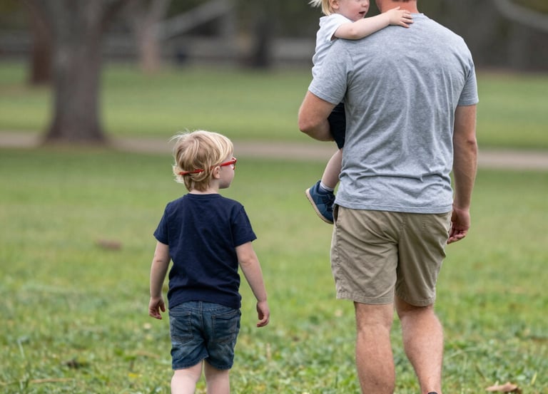 A father playing with his children in a sunny park, smiling and engaged.
