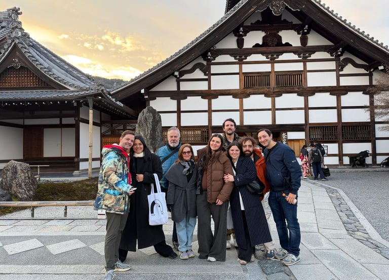 A group of tourists smiling in front of a traditional Japanese temple at sunset in Kyoto.