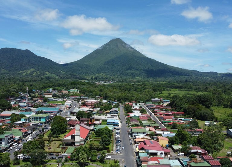 Aerial view of La Fortuna town with the iconic Arenal Volcano in the background under a blue sky.