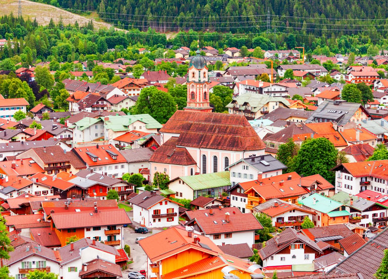 Aerial view of Mittenwald, Germany, featuring red-roofed houses and the St. Peter and Paul church in the Bavarian Alps.