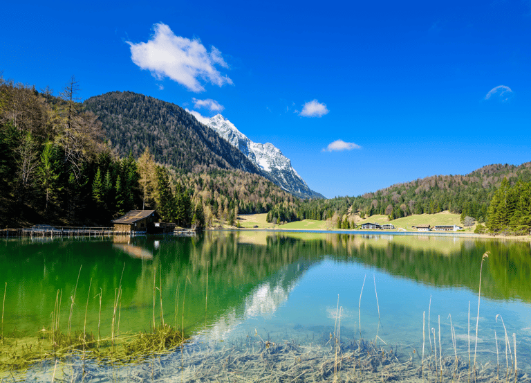 Scenic view of a crystal clear alpine lake in the mountains with a rustic wooden hut and pine forest.