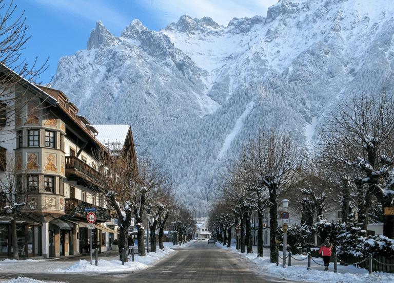 Snow-covered street in Mittenwald, Germany, with traditional Bavarian architecture and Karwendel Alps.