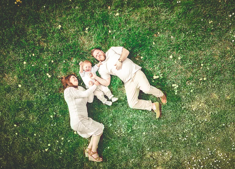Aerial view of a happy family with a baby lying on green grass in a park.