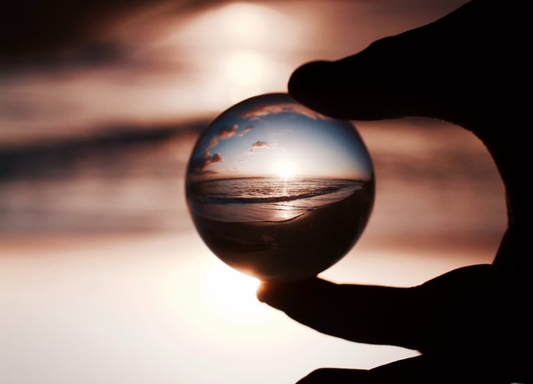 Des doigts tenant une boule de cristal reflétant avec clarté un coucher de soleil sur la mer