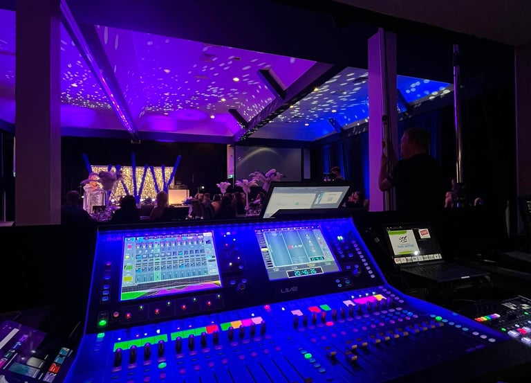 Professional digital audio mixing console at a live event with purple stage lighting.
