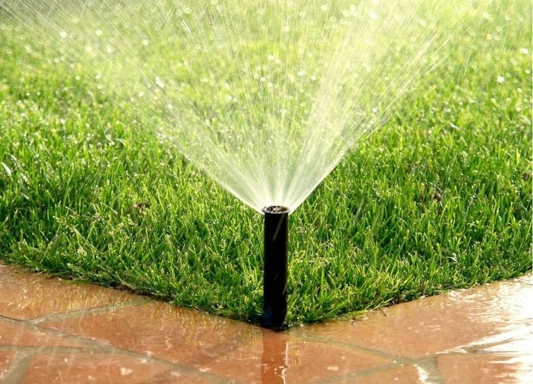 Close-up of a pop-up sprinkler head watering a lush green lawn near a stone patio.