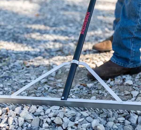 Close-up of a grading rake leveling a gravel base for a stable interlocking stone foundation.