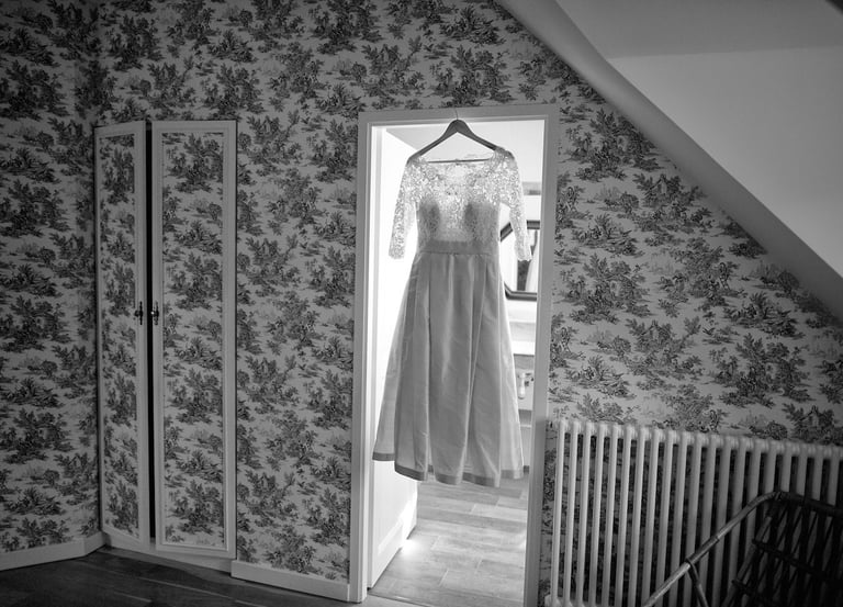 une robe de mariee est suspendue dans l'encadrement d'une porte.