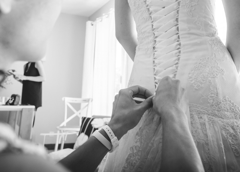 seance d'ajustement de robe de mariée: vue sur les mains de la couturière qui ajuste le laçage.