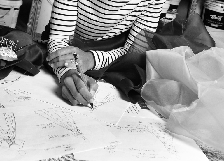 Creatrice qui dessine des robes de mariées, entourée d'échantillons de tissus