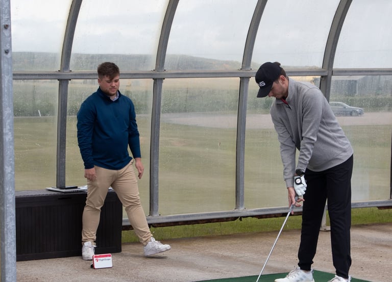 A golf coach in Aberdeen gives a full swing lesson at the driving range, using a launch monitor to evaluate student's swing