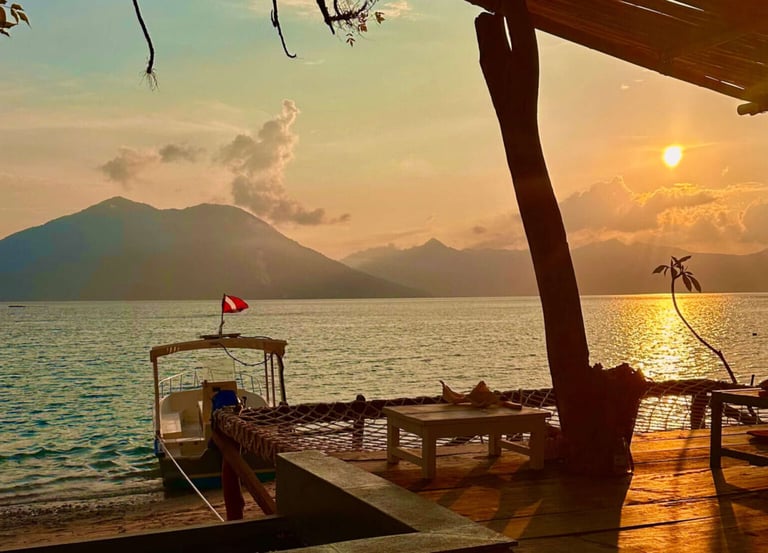 Tropical beach sunset at a resort with a docked boat and mountain views over the calm ocean.
