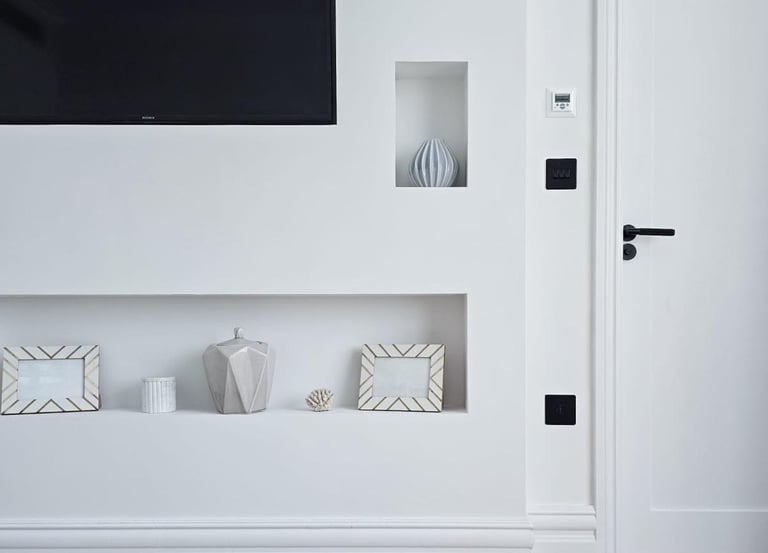 Minimal, white living room with a tv and small alcoves containing ornaments and picture frames