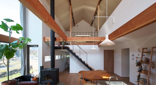 Modern open-plan living area featuring vaulted ceilings, exposed wood beams, and a wood-burning stove.