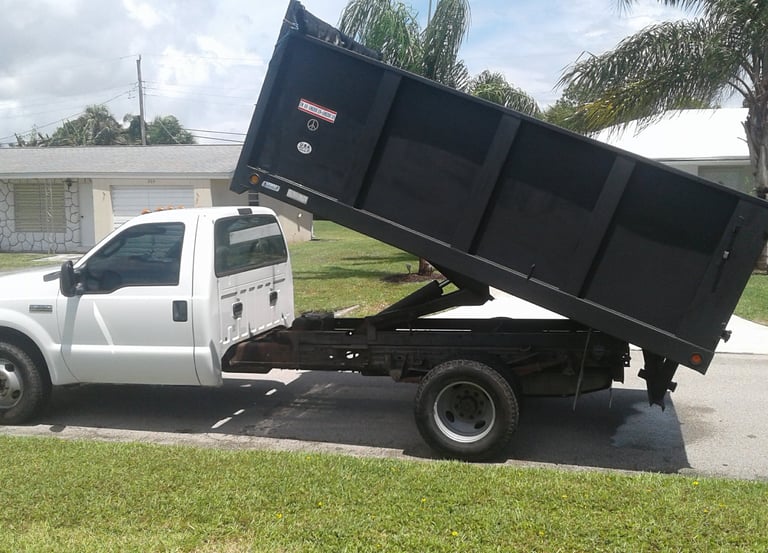 a white truck with a black dumpster sitting on the side of a driveway