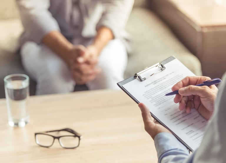 Zwei Personen in einer Psychotherapiesitzun. Der Psychotherapeut macht sich Notizen.