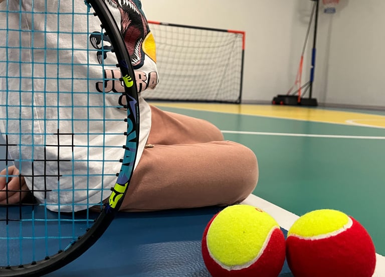 Primo piano di una racchetta da tennis e due palline rosse e gialle su un campo multisport nella palestra Move 2 Grow a Milan