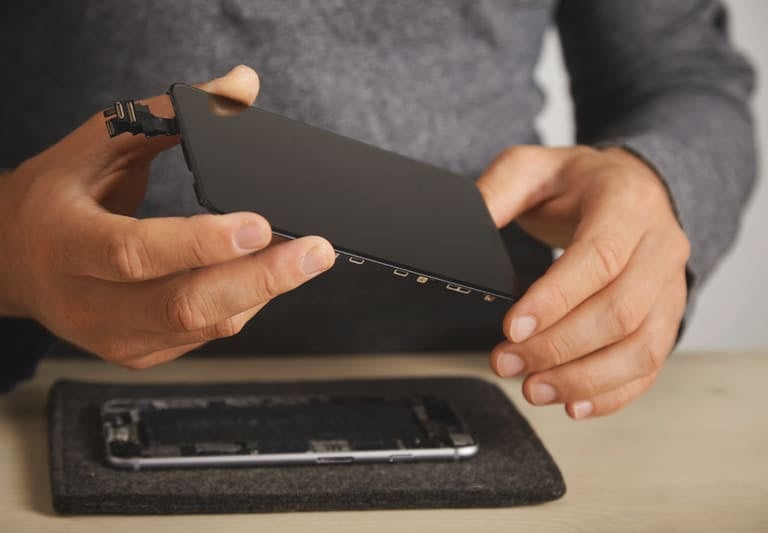 Técnico sosteniendo una pantalla de repuesto para smartphone durante un servicio de reparación