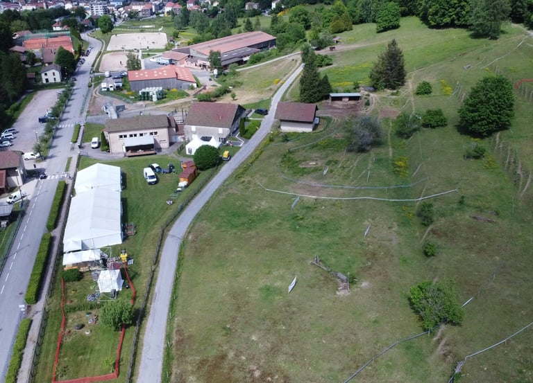 Aerial view of a rural equestrian center and farm buildings next to a grassy hill and paved road.
