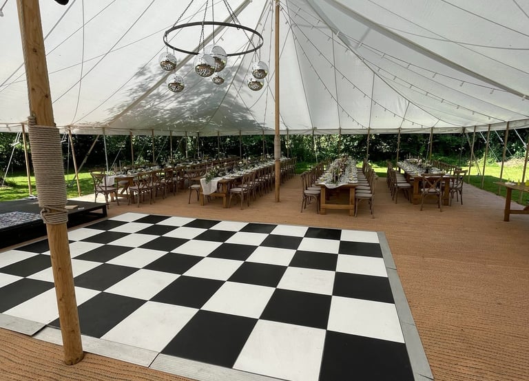 Elegant outdoor wedding marquee with a checkered dance floor and rustic wooden banquet tables.