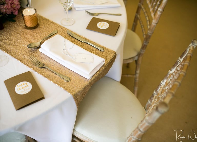 Elegant wedding table setting with gold sequin runner, white linen napkins, and silver cutlery.