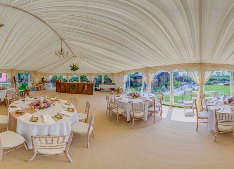 Elegant wedding marquee interior with draped ceiling, round dining tables, and chiavari chairs.