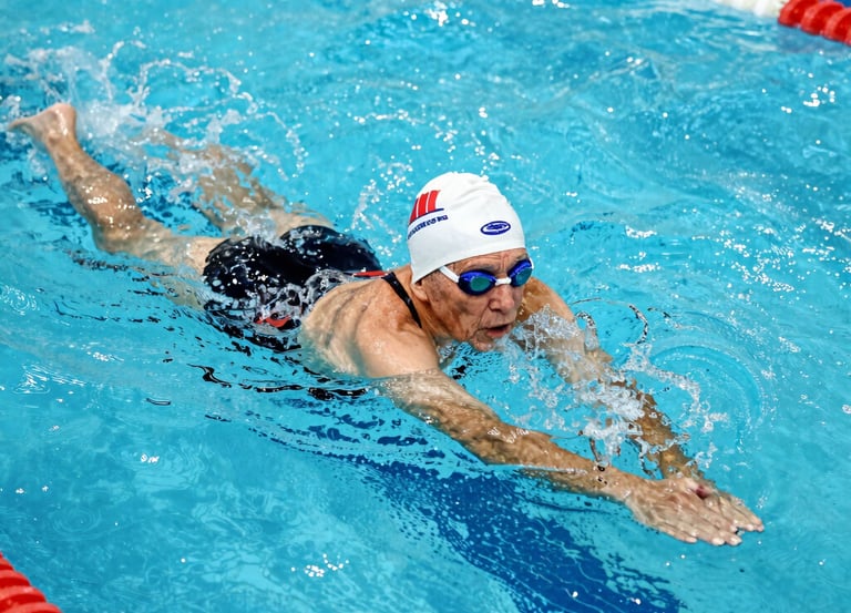 A group of smiling seniors participating in a gentle aquatic exercise session in a bright indoor pool.