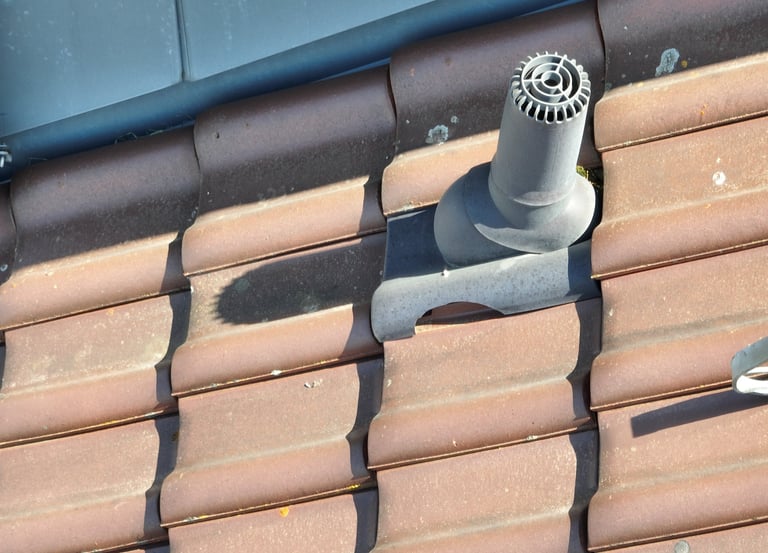 A grey ventilation pipe installed on a brown ceramic tile roof for attic exhaust.