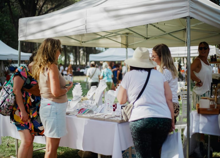 Clientes explorando exhibiciones de joyería artesanal en un mercado de artesanos al aire libre bajo 