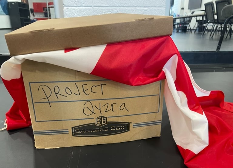 A cardboard file box with Project Qyzra written on it and a Canadian flag sticking out under the lid