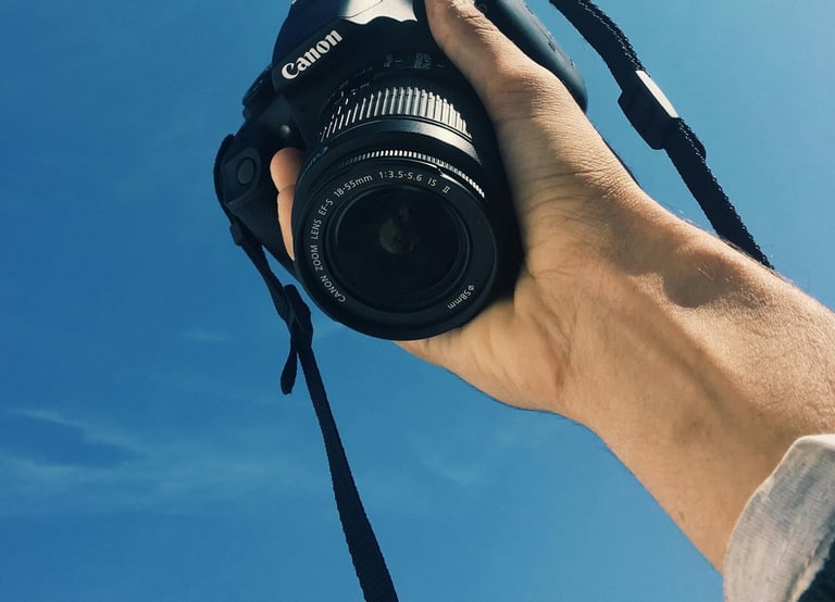 a person holding a camera and taking a picture with a bright blue sky