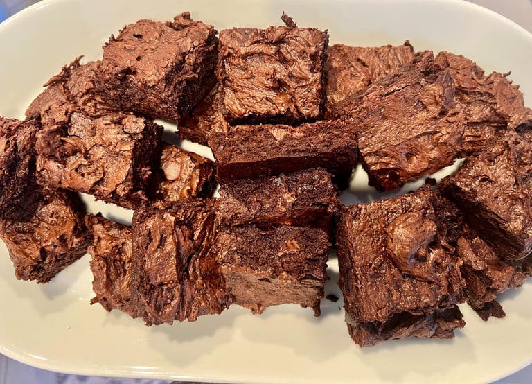 A white plate filled with squares of rich, fudgy chocolate brownies featuring a crinkle top.