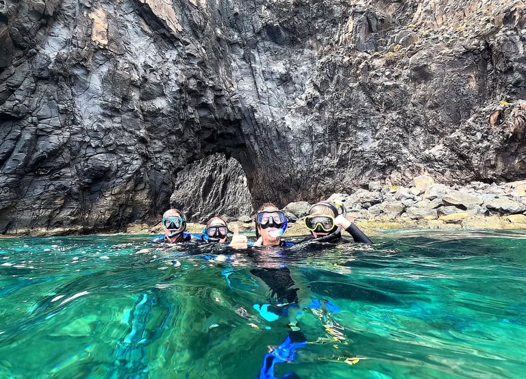 Group of snorkelers in green water in front of a volcanic rock arch at Ponta de São Lourenço, Madeira