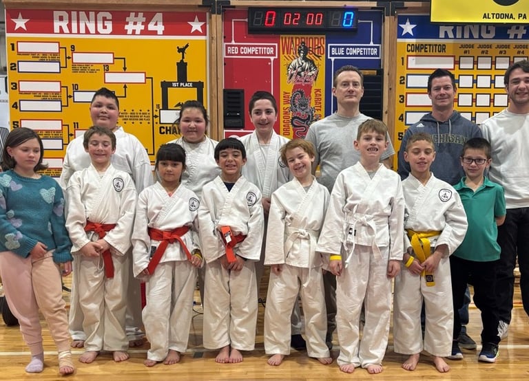 A youth karate tournament group standing in front of competition brackets and a scoreboard in Altoona, PA.