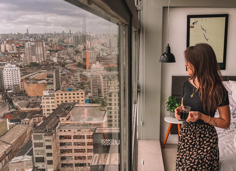 Uma pessoa em pé com uma xícara de café nas mãos, enquanto avista a cidade de São Paulo do topo.
