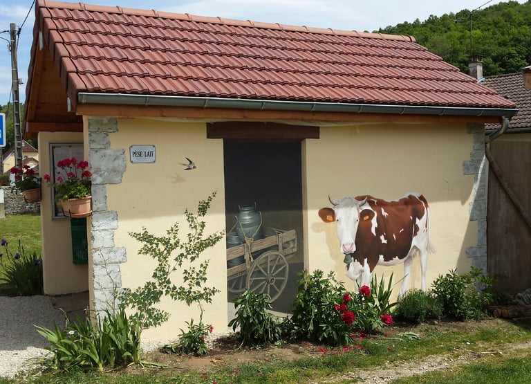 Fresque murale sur façade comporte une fausse porte, une vache et un lierre peints.
