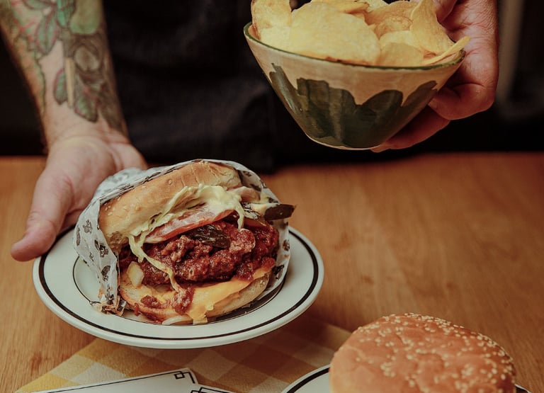 Dan holding a Winnipeg Fat Boy style burger and chips over a table.