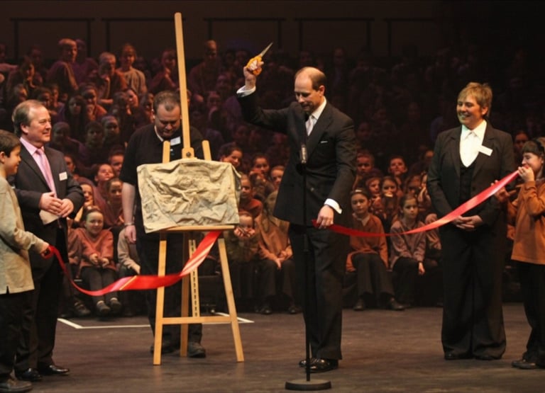 Prince Edward cutting a red ribbon with scissors during an official plaque unveiling in Shrewsbury 